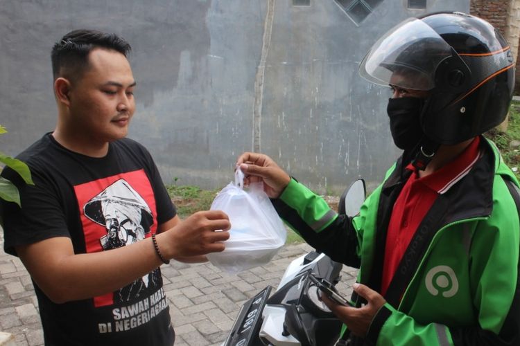 Driver Gojek Ubadillah saat memberikan makanan pada warga yang pesan melalui aplikasi Go Food di Jember