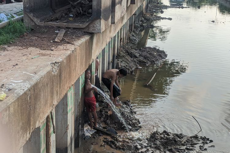 warga bergantian memanfaatkan semburan air di Jalan Boulevard BGR Perintis Kemerdekaan, Kelapa Gading Barat, Jakarta Utara, Selasa (21/1/2020)