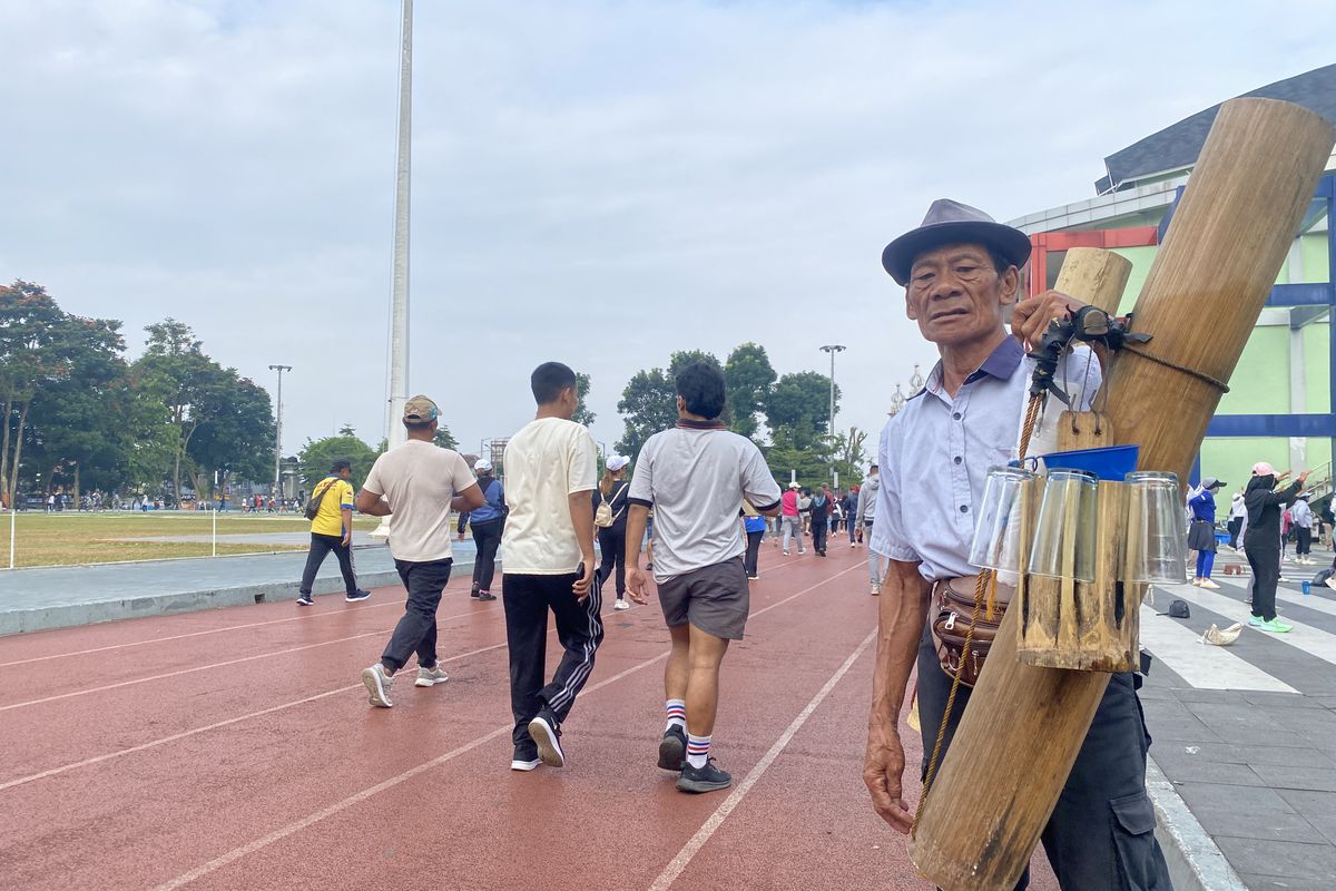 Asep tengah berdiri dengan memilkul bambu yang berisi air lahang untuk dijual di area Lapang Merdeka Kota Sukabumi.