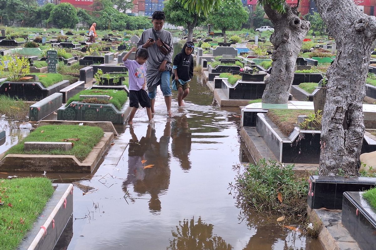 Peziarah di makam TPU Semper, Clincing, Jakarta Utar, terobos genangan banjir untuk menuju makam. Senin (4/3/2024).