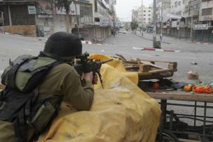Seorang prajurit Israel tengah mengarahkan senjatanya dalam sebuah bentrokan dengan warga Palestina di kota Hebron, Tepi Barat pada 17 Maret 2014, menyusul aksi unjuk rasa warga yang mendukung Presiden Mahmoud Abbas.