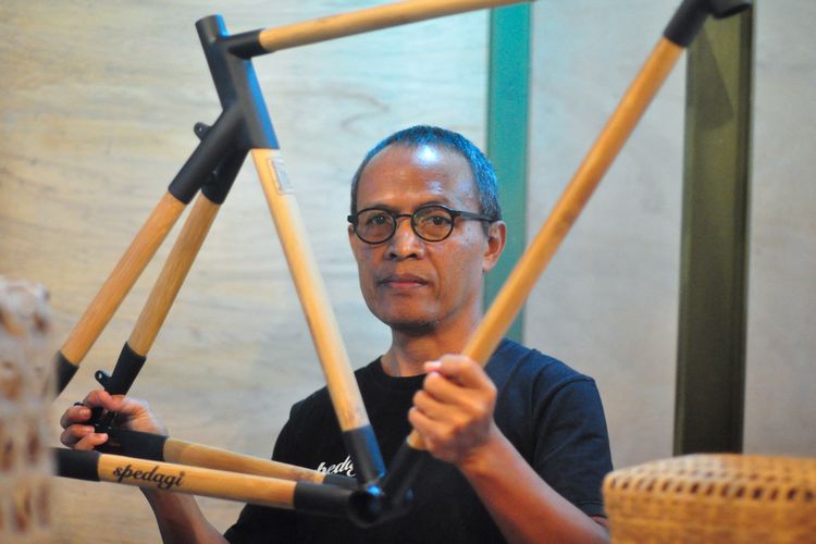 This picture taken on June 18, 2022 shows Indonesian designer Singgih Susilo Kartono posing with a bamboo bicycle frame he crafted at his workshop in Temanggung, Central Java. - Kartono is using his sustainable bike craftsmanship to bring jobs to locals and show Indonesian villagers they can use the environment around them. (Photo by DAFFA RAMYA KANZUDDIN / AFP)