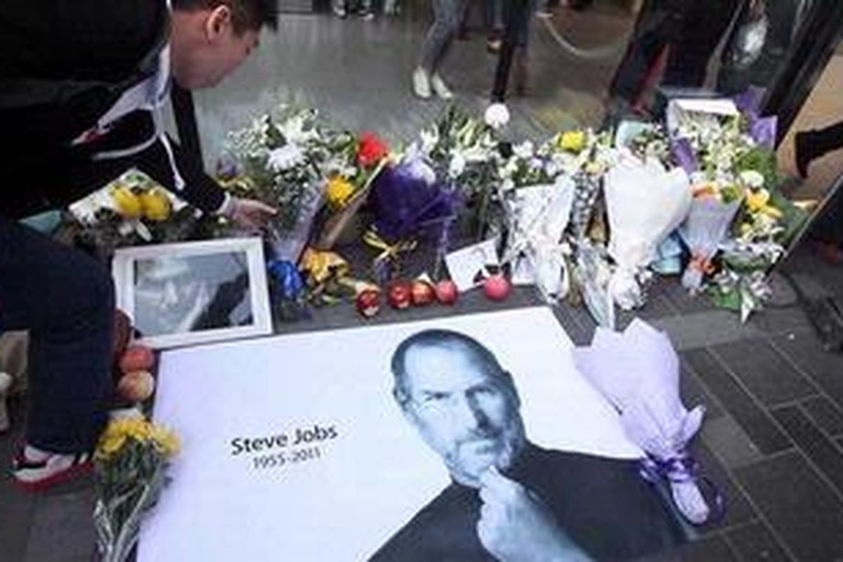 Seorang pria  menempatkan sebuket bunga anyelir putih di samping  sebuah foto Steve Jobs  di luar toko Apple di Beijing, China, Kamis (6/10/2011).