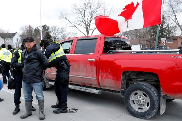 Polisi menahan seorang pengunjuk rasa ketika mereka membersihkan demonstran yang menentang mandat vaksin Covid-19 yang memblokir pintu masuk ke Jembatan Duta Besar di Windsor, Ontario, Kanada, pada 13 Februari 2022.
