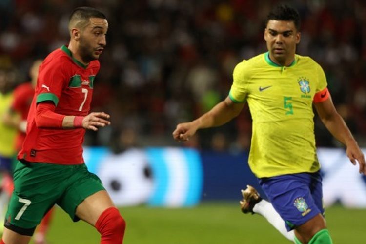 Gelandang timnas Maroko, Hakim Ziyech (kiri), dikawal oleh gelandang timnas Brasil, Casemiro, dalam laga uji coba Maroko vs Brasil yang digelar di Stadion Ibn Batouta, Tangier, pada Minggu (26/3/2023). (Foto oleh: Fadel Senna / AFP)