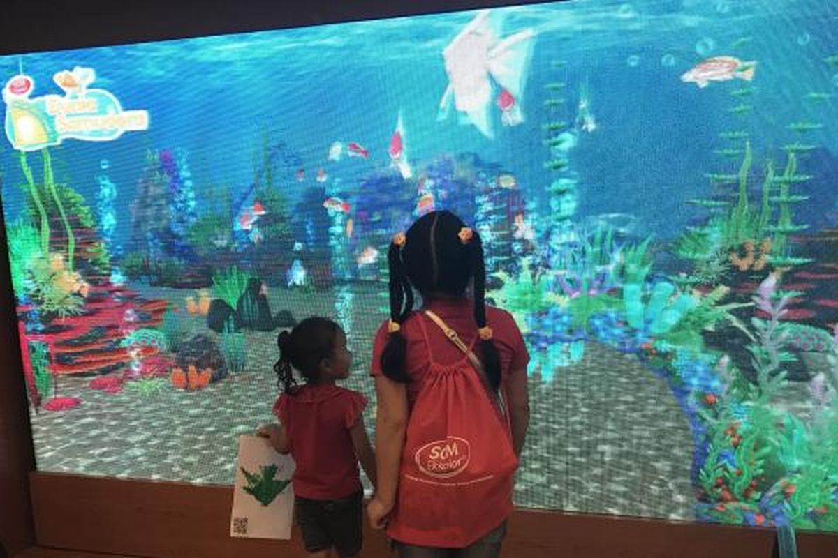 Dua orang anak sedang menyaksikan ikan hasil warnaannya berenang di layar digital dalam acara 