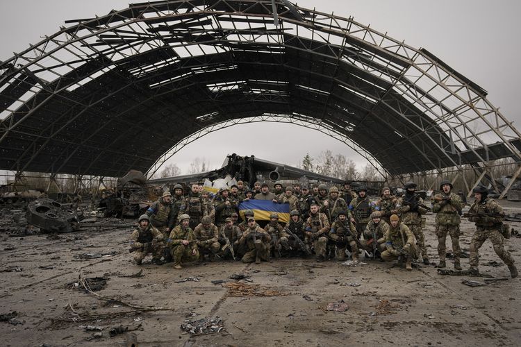 Pasukan tentara Ukraina berfoto dengan latar belakang bangkai Antonov An-225 Mriya, pesawat terbesar di dunia yang hancur dalam perang Rusia vs Ukraina di bandara Hostomel, Ukraina, Sabtu (2/4/2022).