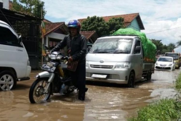 Rofiq (53) menuntun kendaraannya saat melewati Jalan Raya Sapan, Desa Tegalluar, Kecamatan Bojongsoang, Kabupaten Bandung. Rabu (8/3/2017).
