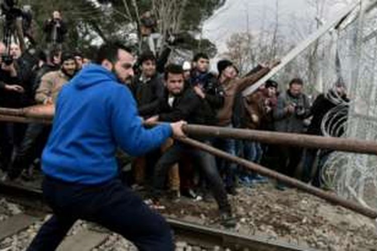 Sekelompok migran menerobos pagar kawat di perbatasan Macedonia-Yunani dengan menggunakan batang besi.