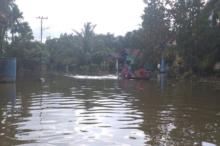 Warga mendayung sampan di lokasi banjir yang merendam akses jalan penghubung desa di Desa Tanjung Balam, Kecamatan Siak Hulu, Kabupaten Kampar, Riau, Minggu (29/12/2019).