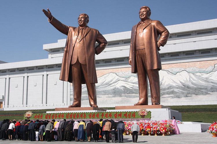 Warga Korea Utara membungkuk di depan patung perunggu Kim Il Sung dan putranya, Kim Jong Il di Kota Pyongyang.
