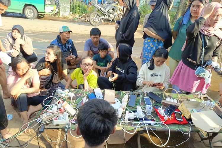 Puluhan warga Kampung Lamajang, Desa Citereup, Kecamatan Dayeuhkolot, Kabupaten Bandung mengantre untuk mengisi baterai HP miliknya di bengkel milik salah seorang warga yang membuka jasa charge HP, Jumat (12/1/2024)