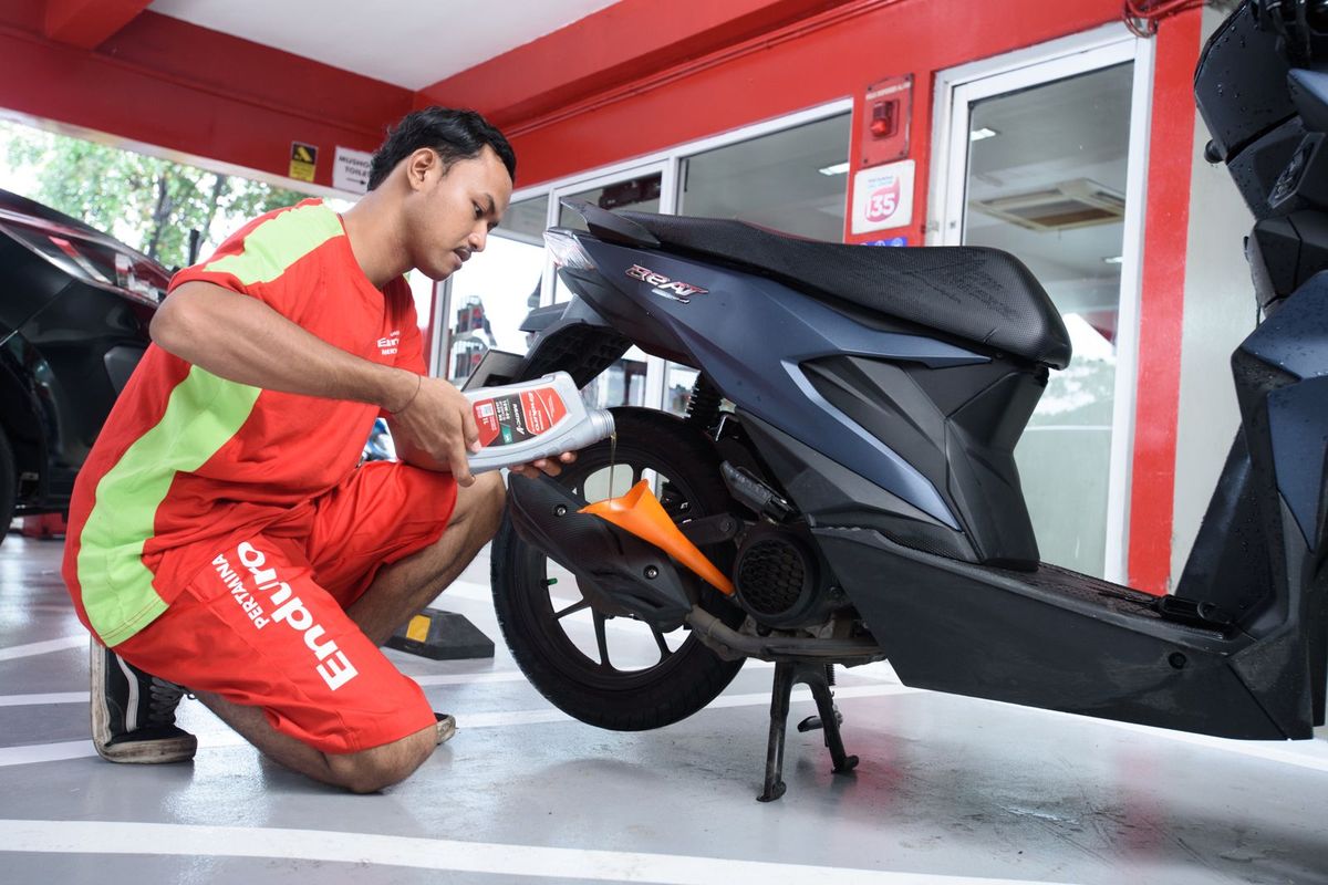 Ilustrasi pekerja sedang menuangkan oli Pertamina ke dalam mesin motor.