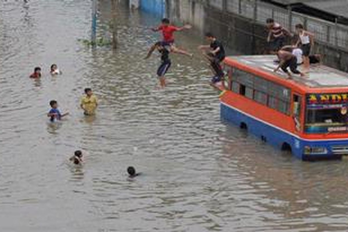 Bagi anak-anak banjir justru menjadi  tempat untuk bermain, seperti terlihat di jalan arteri Puri Kembangan menuju Rawa Buaya, sejumlah anak melompat dari atas metromini ke dalam genangan air, Jumat (18/1/2013).