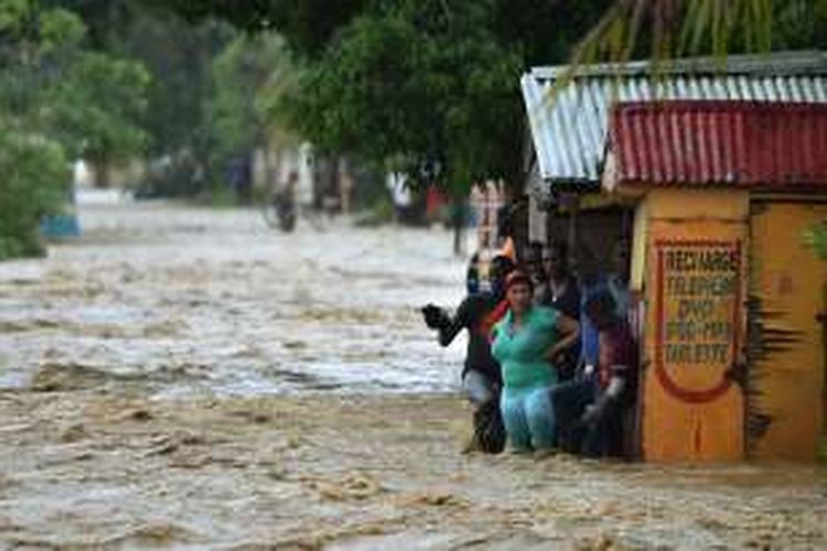 Warga mencoba menyeberangi jalanan yang dilanda banjir akibat Sungai  La Rouyounne di sebelah selatan kota Port-au-Prince, Haiti. Sungai ini meluap akibat terjangan badai Matius yang sudah menewaskan 108 orang.