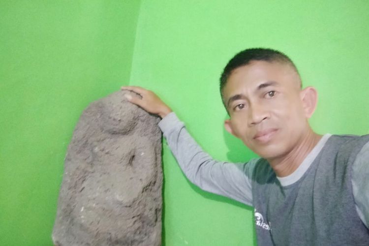 Petugas lapangan Disparporabud Kabupaten Nganjuk, Aris Trio Effendi, memegang arca kuno yang ditemukan di Sendang Prajunan Desa Sumberagung, Kecamatan Gondang, Nganjuk. Kini arca tersebut diamankan di balai desa seempat. Foto: Disparporabud Nganjuk.