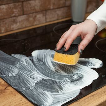 Ilustrasi membersihkan kompor induksi menggunakan spons basah.