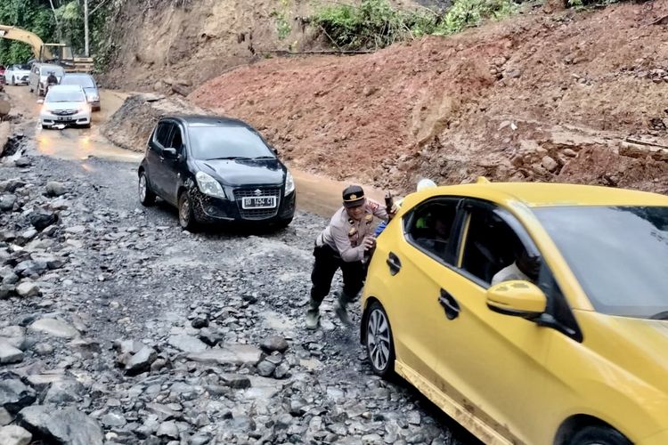 Anggota kepolisian Polres Lampung Barat mendorong mobil yang kesulitan melintasi jalan di KM 17 Jalinbar akibat longsor, Minggu (14/4/2024).