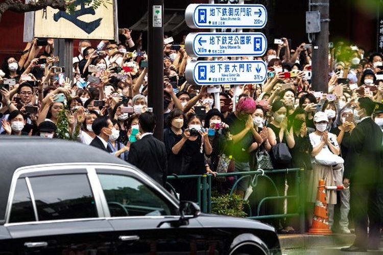 Orang-orang menyaksikan mobil jenazah yang mengangkut jenazah mantan perdana menteri Jepang Shinzo Abe saat meninggalkan Kuil Zojoji di Tokyo pada Selasa (12/7/2022). 