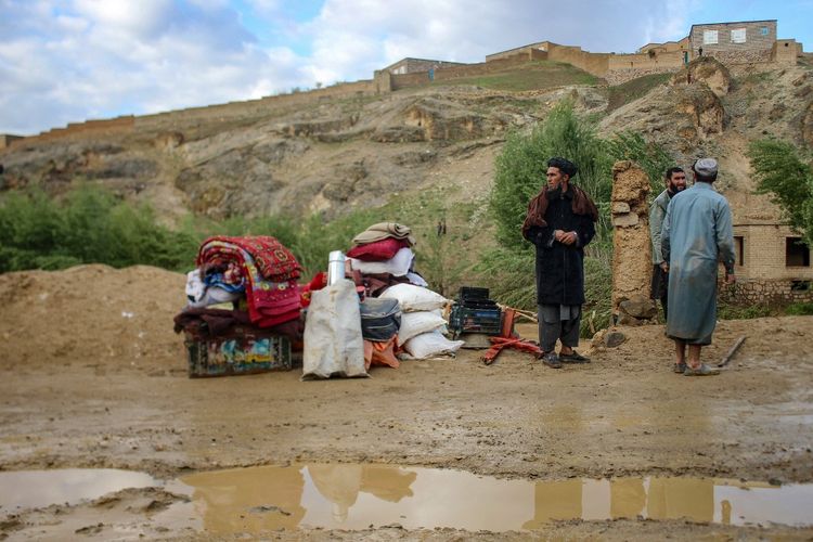 Pria Afghanistan berdiri di samping barang-barang mereka yang disimpan di dekat rumah yang rusak setelah banjir bandang menyusul hujan lebat di Firozkoh, provinsi Ghor pada 18 Mei 2024.