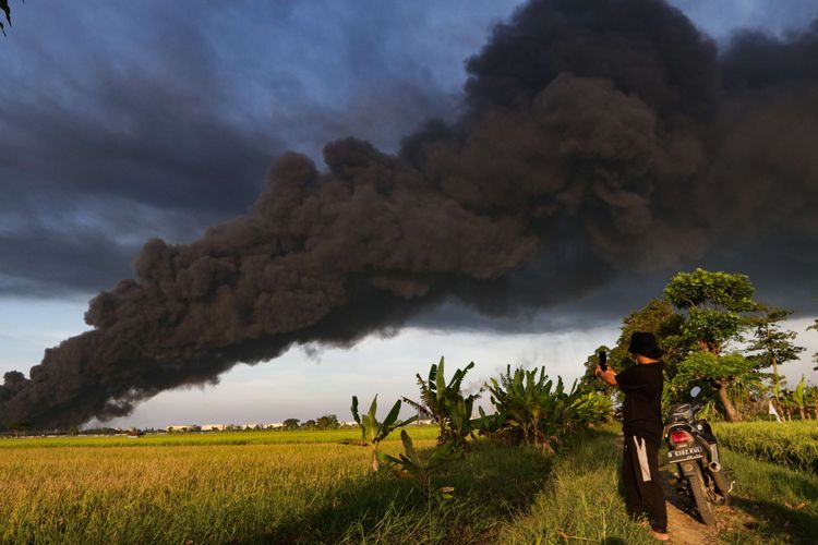 Warga menyaksikan kebakaran kilang minyak milik Pertamina RU VI di Balongan, Indramayu, Jawa Barat, dari kejauhan, Senin (29/3/2021).  Tangki di kilang minyak milik Pertamina ini terbakar pada Senin, pukul 00.45 WIB.