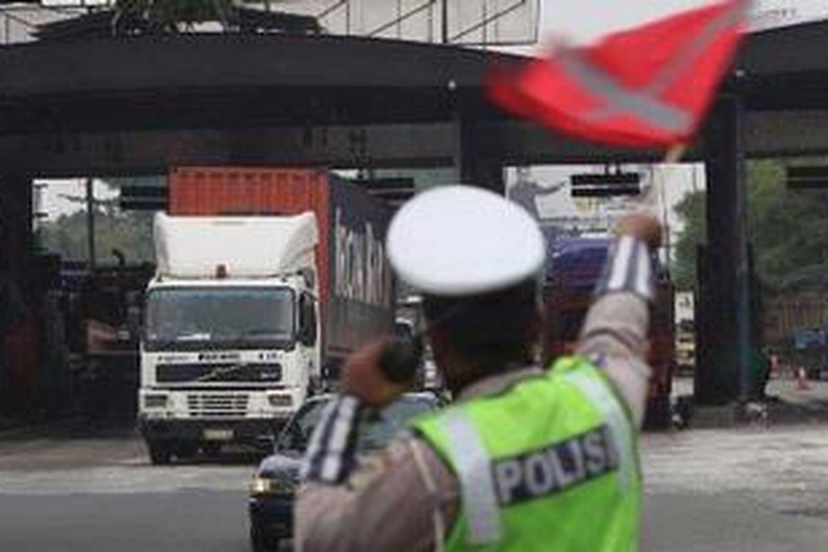 Anggota kepolisian, Aiptu Hadi S mengarahkan truk pengangkut barang agar melintas menuju arah Tanjung Priok seusai membayar di Pintu Tol Tomang, Jakarta Barat, Jumat (20/5/2011). Hari itu, kebijakan pembatasan truk angkutan barang untuk melintas di tol dalam kota tetap diberlakukan seperti biasa.
