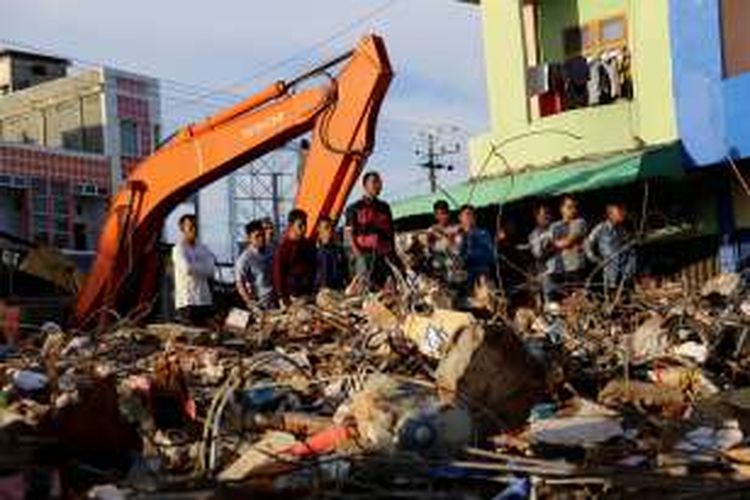 Warga menyaksikan aparat TNI/Polri bersama tim Basarnas mencari korban yang tertimbun bangunan pasar Meureudu yang roboh akibat bencana gempa di Kecamatan Meureudu, Kabupaten Pidie jaya, Aceh, Kamis, (8/12/2016). Sebagian korban sudah teridentifikasi dan sebagian lagi masih dalam proses pendataan serta korban luka sendiri berjumlah 128 orang luka berat, dan 489 orang luka ringan, 86 unit rumah, 105 ruko, 13 unit masjid rusak berat.