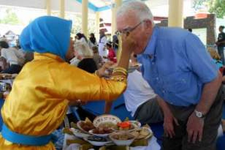 Seorang wisatawan kapal pesiar tengah disuapi oleh wanita yang menyuguhkan makanan dalam acara kande-kandea, di Baubau, Sulawesi Tenggara, Rabu (24/2/2016).