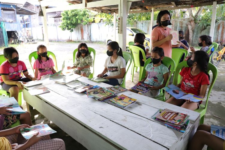 Belvi, seorang Bidan Desa di Puskesmas mendirikan TBM Pelita Kanaan, di Kecamatan Malinau, Kalimantan Utara sedang mendampingi anak-anak belajar membaca.