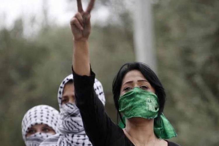 Perempuan Palestina, dengan menutup mulut menggunakan syah Hamas, emngacungkan tanda victory saat bentrokan dengan tentara Israel di Beit El, dekat ramalla, Tepi Barat, 10 Oktober 2015.