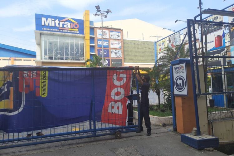 Seorang petugas sekuriti di Toko Mitra 10, Jalan Raya Sholeh Iskandar, sedang menutup pintu gerbang area toko dengan spanduk, Kamis (18/6/2020). Seluruh karyawan Toko Mitra 10 Bogor yang berstatus ODP menjalani tes swab setelah tiga orang karyawan di sana dinyatakan terkonfirmasi positif Covid-19.