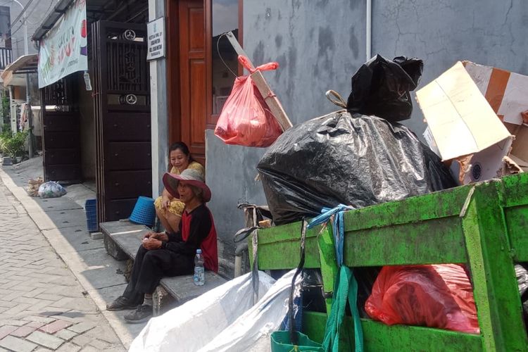 Pak Markan sedang beristirahat di pinggir jalan Gang 1 Lidah Wetan sambil berteduh dan berbincang dengan warga sekitar yang memberikannya minuman dan kopi hitam.