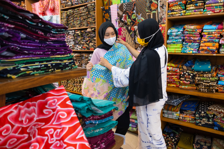Pembeli sedang mengamati motif dan bahan kain di toko. 