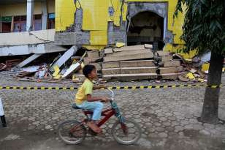 Warga melintas di depan bangunan pondok pesantren di bawah Lembaga Pendidikan Islam Ma'hadal Ulum Diniyah Islamiyah roboh akibat gempa di Samalanga, Kabupaten Bireun, Aceh, Sabtu (10/12/2016). Presiden joko Widodo berjanji untuk secepatnya dilakukan pembangunan kembali dan  akan ditangani oleh Kementerian Pekerjaan Umum dan Perumahan Rakyat.