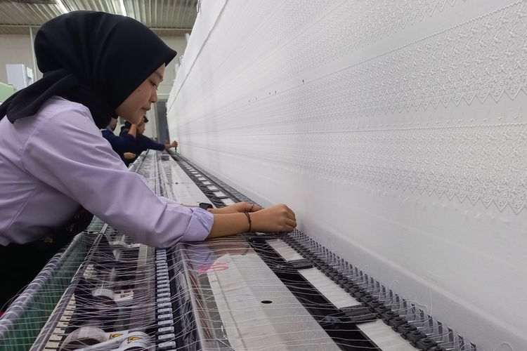 Ilustrasi karyawan pabrik tekstil tengah bekerja merapikan benang di mesin produksi. 