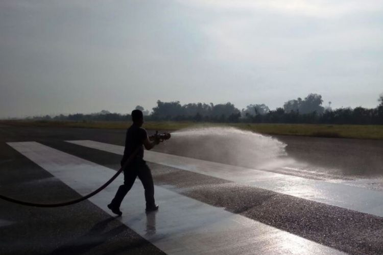 Petugas menyiram landasan pacu Bandara Sultan Malikussaleh, Aceh Utara, yang dipenuhi debu abu vulkanik Gunung Sinabung, Selasa (20/2/2018)