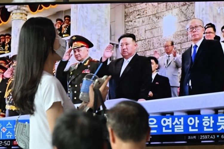 Seorang perempuan berjalan melewati layar televisi di sebuah stasiun kereta api di Seoul, yang menayangkan siaran berita pemimpin Korea Utara Kim Jong Un menghadiri parade militer di Pyongyang untuk memperingati 70 tahun gencatan senjata Perang Korea, Kamis (27/7/2023) malam.