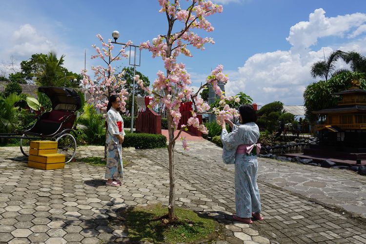 Pengunjung menggunakan baju sewa kimono dan berfoto di area taman sakuran.