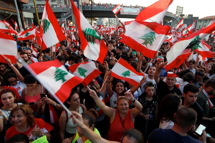 Demonstran melambaikan bendera Lebanon dalam aksi unjuk rasa menentang pemerintah di jalan raya Jal el-Dib, pada 21 Oktober 2019.