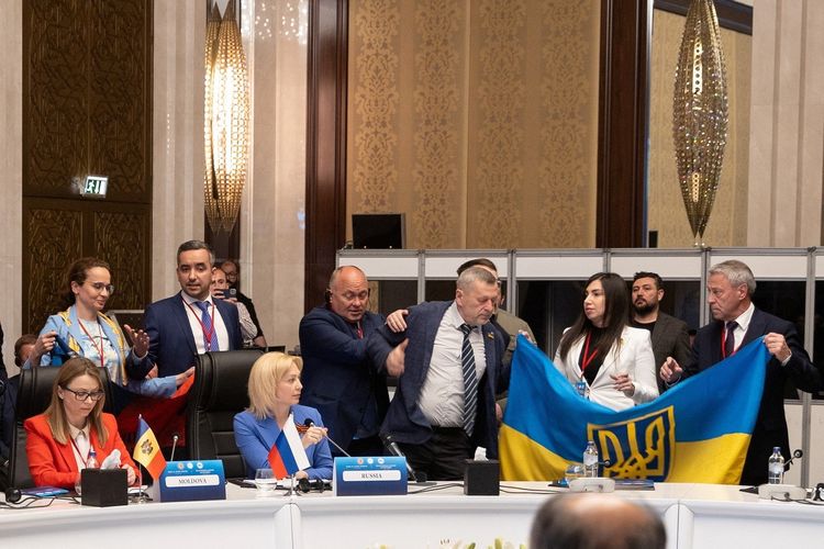 Anggota delegasi Ukraina mengibarkan bendera nasional mereka di samping Olga Timofeeva, wakil kepala delegasi Rusia, untuk mengganggu pidatonya selama pertemuan Majelis Parlemen Kerjasama Ekonomi Laut Hitam (PABSEC) di Ankara, Turkiye pada Kamis (4/5/2023). 