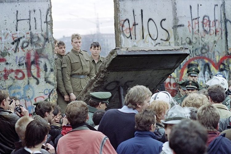 Warga Berlin Barat berkumpul di depan Tembok Berlin. Pada saat yang sama, para penjaga perbatasan dari Jerman Timur membuka titik persimpangan baru di antara dua wilayah tersebut. Foto ini diambil pada tanggal 11 November 1989. 