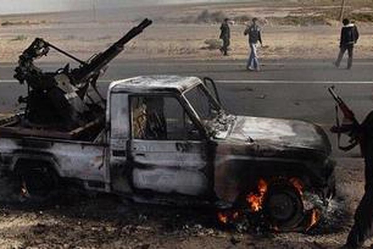 Seorang pemberontak Libya menenteng senjata AK-47 saat ia berjalan dekat kendaraan tempur pasukan pro Moammar Khadafi di kota Brega, Rabu (2/3/2011)