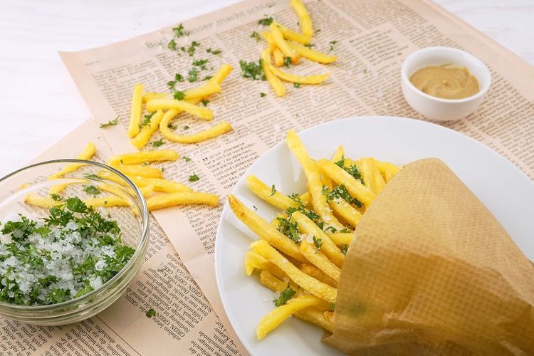 Ilustrasi kentang goreng dengan taburan garam dan daun peterseli. 