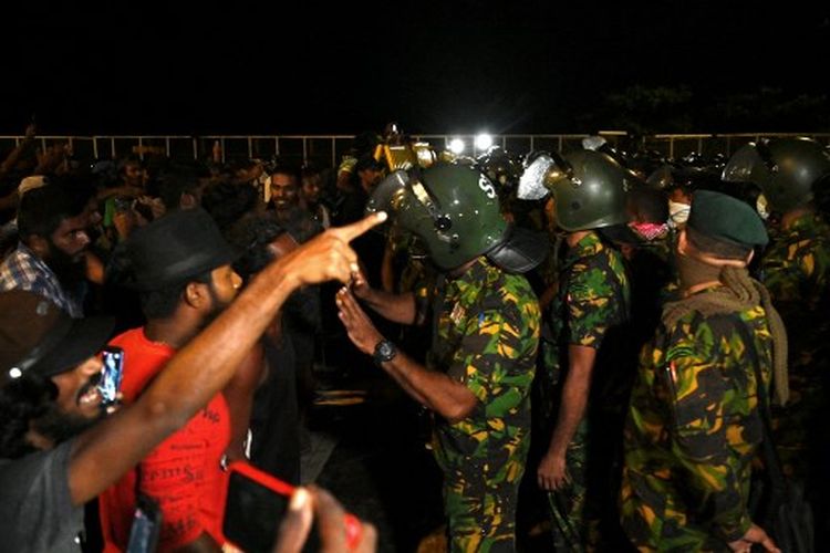 Pengunjuk rasa anti-pemerintah (kiri) berbicara dengan anggota pasukan keamanan Sri Lanka di lokasi kamp protes di depan Sekretariat Presiden di Colombo pada 22 Juli 2022.  Ratusan tentara dan polisi Sri Lanka menggerebek markas anti-pemerintah utama kamp protes di ibu kota pada awal 22 Juli dan mulai merobohkan tenda-tenda aktivis yang tidak bersenjata, kata seorang wartawan AFP. \" data-caption-en=