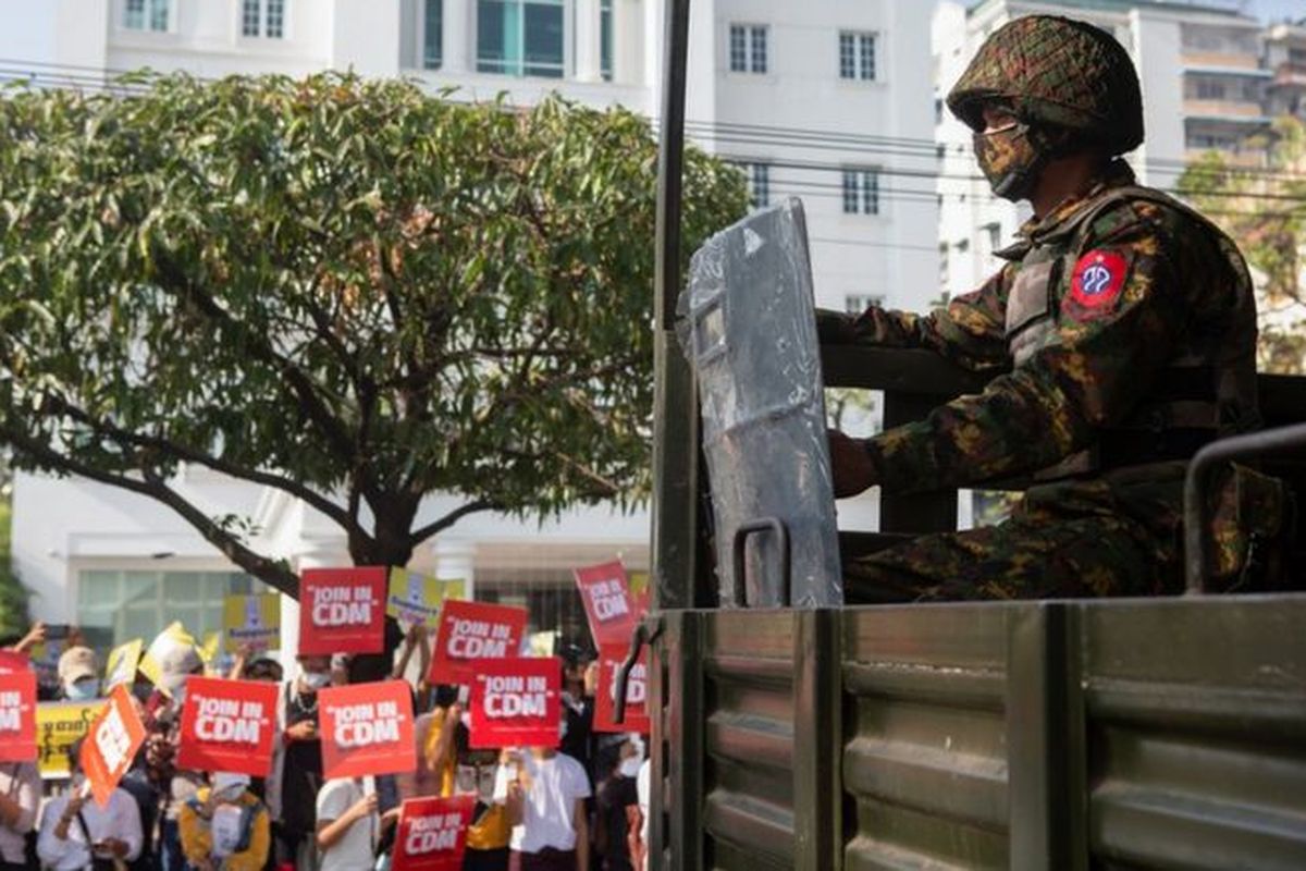 Civilian protesters hold up Join in (the) CDM (Civil Disobedience Movement) banners in front of a soldier in Yangon, Myanmar