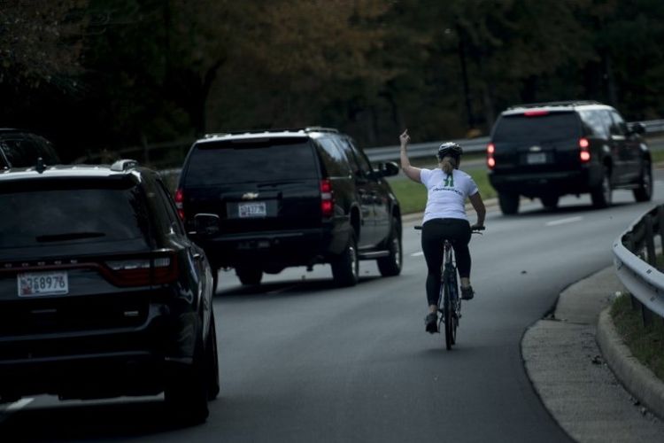 Seorang perempuan yang tengah mengendarai sepeda mengacungkan jari tengahnya ke arah rombongan Presiden AS Donald Trump yang baru saja selesai bermain golf.