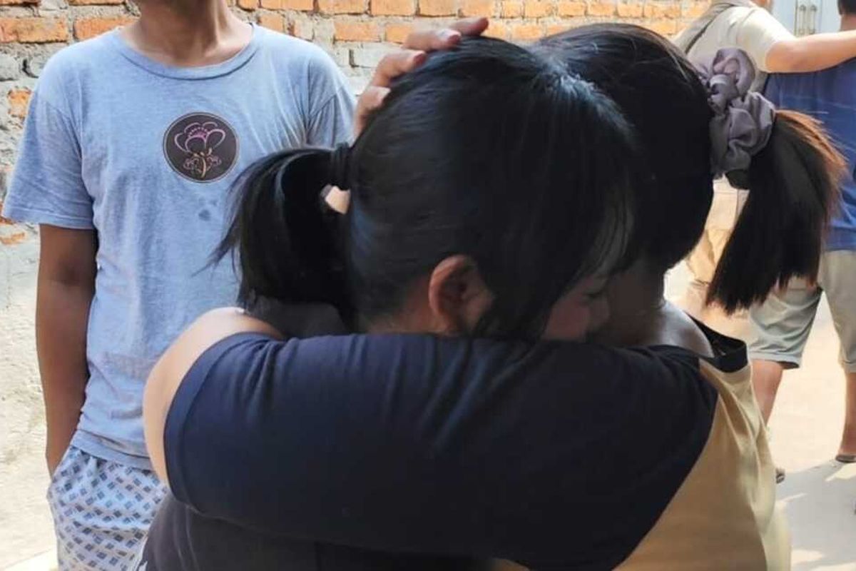 Neisya Fuji Lestari (Hoodie hitam) menangis dan menunjukkan foto ibunya Tasmi, pekerja buruh migran yang meninggal dunia di Malaysia, saat ditemui Kompas.com di rumahnya pada Sabtu (12/7/2025) siang.