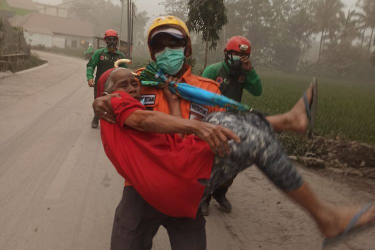 EVAKUASI WARGA: Seorang petugas terlihat tengah mengevakuasi warga saat erupsi Gunung Semeru, Minggu (4/12/2022).
