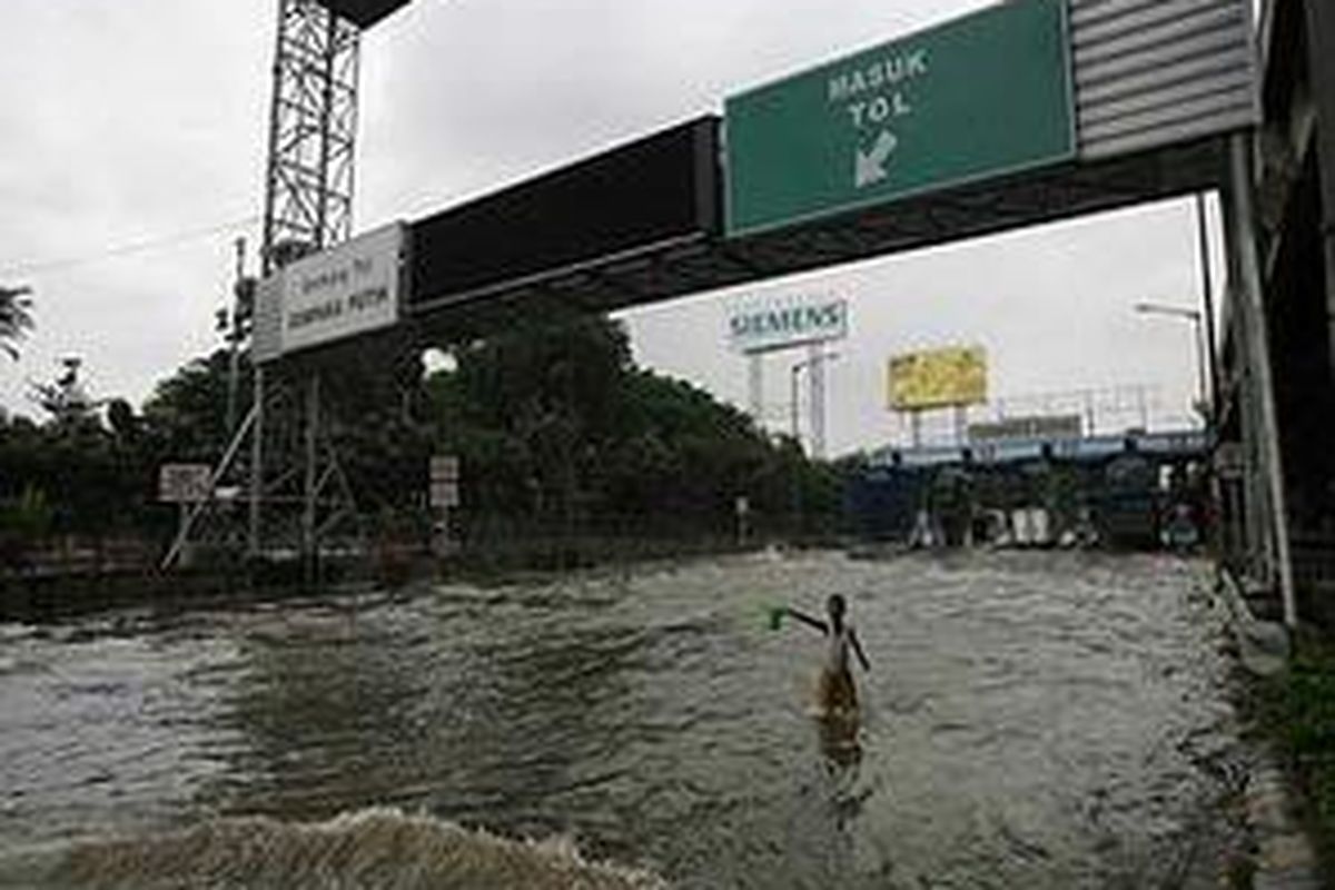 Seorang anak memberi aba-aba dan minta uang sukarela dari pengguna kendaraan yang akan masuk pintu tol Cempaka Putih, Jakarta Pusat, Sabtu (2/2). Meski hujan sudah tidak lagi mengguyur Jakarta dan sekitarnya namun genangan air masih merendam sejumlah kawasan.