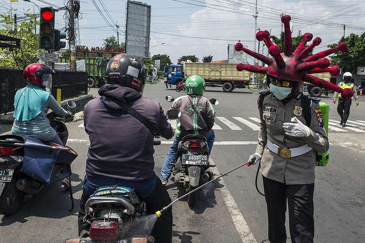 Anggota polisi memakai helm berbentuk virus corona melakukan imbauan dan penyemprotan cairan disinfektan pada kendaraan di jalanan di daerah Mojokerto, Jawa Timur, Jumat (3/4/2020). Cara unik ini dilakukan oleh sejumlah anggota dari Polres Mojokerto dalam upaya menekan penyebaran virus corona atau penyakit Covid-19 yang tengah merebak di Tanah Air.